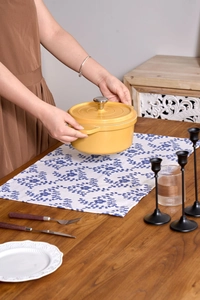 Detail of yellow enamel cast iron pot with silver handle on blue floral table runner