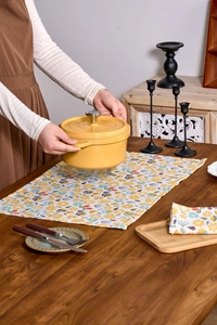 Detail of yellow enamel cast iron pot with floral cloth placemat on a wooden table
