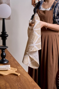 Detail of cotton linen napkin with brown diamond pattern near glassware and wooden tray