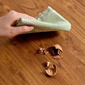 Modern light green floral linen napkin used for cleaning walnut crumbs on a wooden table