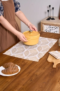 Detail view of a yellow round enamel cast iron pot being placed on a dining table cloth