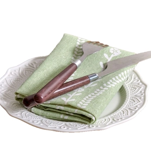 Green floral cotton linen napkin on white embossed plate with wooden cutlery set