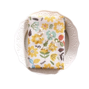Floral cotton linen napkin with yellow wildflowers on white ceramic plate background