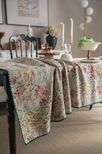 Detail of vintage floral tablecloth featuring green scalloped edges and embroidered patterns