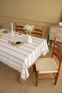 Detail of cream rectangle tablecloth featuring orange wavy embroidery and white tassels