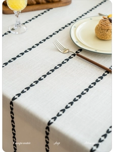 Detail of beige linen tablecloth with black geometric embroidery and tassel edges