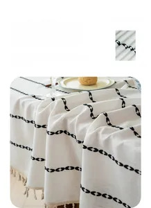 Detail of breathable linen-like tablecloth with black leaf patterns and woven tassels