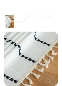 Detail of white linen table runner with black wavy embroidery and cream tassels