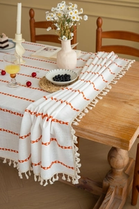 Detail of bohemian cream tablecloth with orange embroidery and handmade tassels