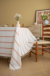 Detailed close-up of cream cotton linen tablecloth with orange heart embroidery and tassels