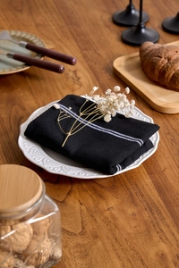 Close-up of black cotton linen napkin with white stripes on a white embossed dinner plate