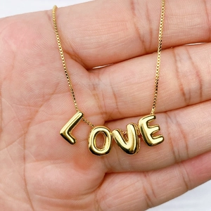 Detailweergave van een vergulde LOVE-hanger aan een doosketting in de hand
