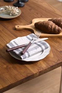 Makro-Detail von Edelstahlbesteck mit Holzgriff auf grau-weißer Gitter-Serviette