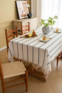 Detailed texture of off-white tablecloth with black vertical leaf stripes and tassels