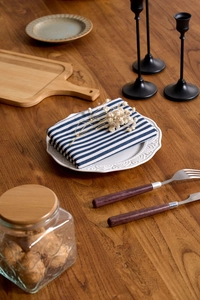 Close-up of blue striped linen napkin folded on a white ceramic plate over wooden table