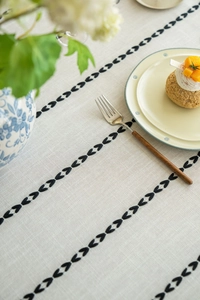 Detailed view of linen tablecloth with black geometric embroidery and rustic tassels