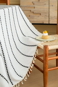 Detail of white cotton tablecloth featuring black heart stripes and elegant fringe tassels