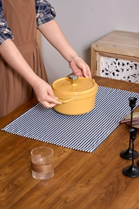 Detail view of a bright yellow enameled cast iron dutch oven set on a blue striped tablecloth