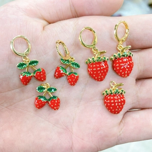 Primo piano di orecchini a fragola e ciliegia in smalto dorato su una mano per la scala