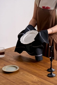 Detail showing a black striped cotton linen napkin with an embossed white ceramic plate