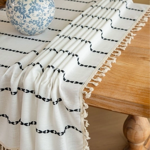 Rectangular boho tablecloth with black leaf embroidery and cream tassels on a wooden table