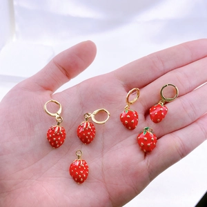 Primo piano di cinque orecchini a fragola rossa con cerchi dorati tenuti in una mano
