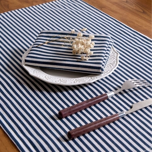 Blue and white striped linen dinner napkins set on a wooden table with white plates