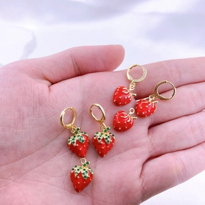 Dettaglio di sei orecchini a fragola rossa con foglie di zircone verde tenuti in mano