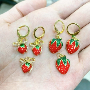 Dettaglio di orecchini a fragola in smalto rosso con fiocco dorato e cristalli in mano