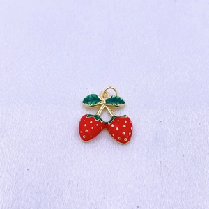 Dettaglio di ciondoli a fragola rossi con semi dorati e finitura in smalto verde