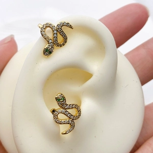 Detailed view of snake-shaped ear cuffs with green gemstone eyes and white pave crystals