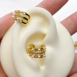 Macro shot of gold ear cuff featuring hollow heart design and faux pearl on a silicone ear