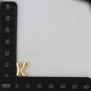 Macro detail of gold 3D bubbly letter K pendant on a measuring scale for DIY jewelry