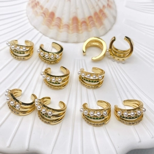Macro detail of triple-layer gold ear cuffs with pearls, green stones, and clear crystals