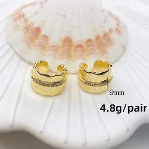 Nahaufnahme goldener Wellen-Ohrklemmen mit Zirkonia auf weißem Muschelhintergrund