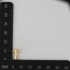 Macro shot of a shiny 18k gold initial T pendant measured on a millimeter scale ruler