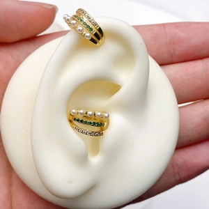Detail of double-layer C-shaped gold ear cuff with white pearls and green gemstones