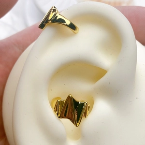 Macro detail of wave and geometric gold plated ear cuffs set on a silicone ear model