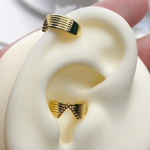 Close-up of minimalist gold-plated wave ear cuffs with parallel groove texture and bead detail