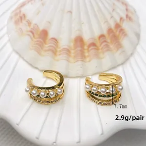 Detail of 18K gold double C ear cuff with white pearls and green zircon on a shell