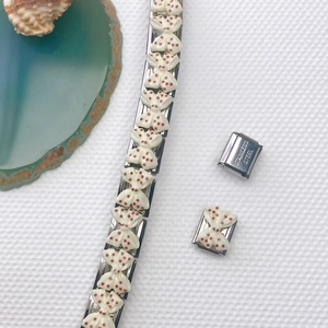 Detailansicht eines Edelstahl-Charm-Armbands mit rosa gepunkteten Schleifenmotiven