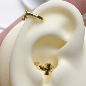 Detailed close-up of a 18K gold plated cross ear cuff with beaded edges on a model ear