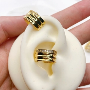 Detailed macro view of U-shaped gold ear cuff with wavy texture and white zircon stones