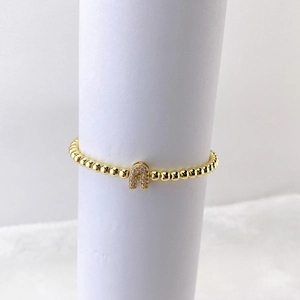 Detalle de una pulsera de cuentas doradas con un colgante de la letra A con micro pavé