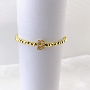 Detalle de pulsera de cuentas doradas con colgante ovalado de circonitas para joyería