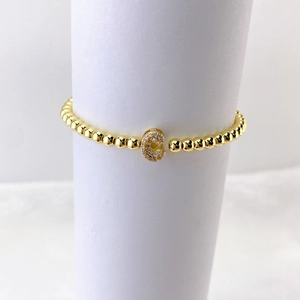 Detalle de pulsera elástica de cuentas doradas con dije de letra C en micro-pavé de cristal