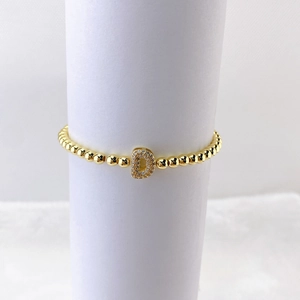 Detalle de pulsera de cuentas doradas con colgante de letra D en circonitas micro-pavé