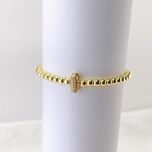 Detalle de pulsera de cuentas doradas con dije ovalado con micropavé de cristales finos
