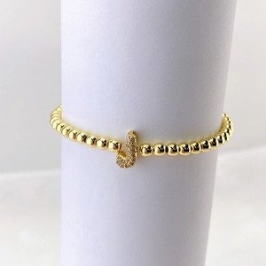 Detalle de pulsera de cuentas doradas con colgante de letra J y circonitas micro-pave
