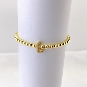 Detalle de la pulsera de cuentas de latón dorado con dije de letra L en micropavé de circonia
